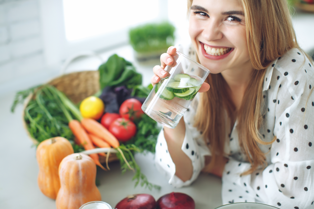 Lachende Frau mit Gemüse vor sich und einem Glas Wasser